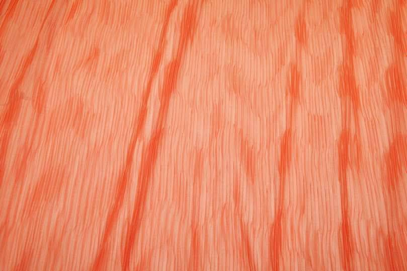 Tessuto chiffon plissettato arancio con pieghettatura regolare a metraggio.